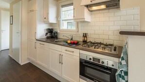 A modern kitchen with white cabinets, a Bosch oven, a gas stove, and a window above the sink. - Well Furnished Mobile Home with Dishwasher near Water (Gasselternijveen)