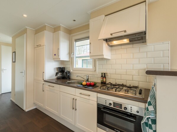 A modern kitchen with white cabinets, a Bosch oven, a gas stove, and a window above the sink. - Well Furnished Mobile Home with Dishwasher near Water (Gasselternijveen)