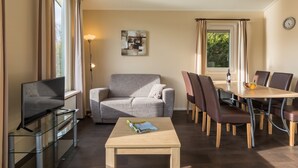 A modern living room with a sofa, a coffee table, a TV, and a dining area with chairs and a table. - Well Furnished Mobile Home with Dishwasher near Water (Gasselternijveen)