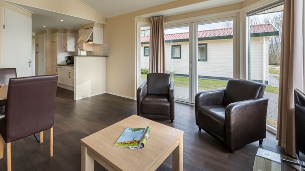 A spacious living room with a dining area, a kitchen, and a sliding glass door leading to a balcony. - Well Furnished Mobile Home with Dishwasher near Water (Gasselternijveen)