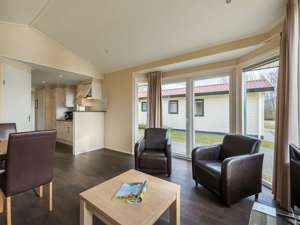 A spacious living room with a dining area, a kitchen, and a sliding glass door leading to a balcony. - Well Furnished Mobile Home with Dishwasher near Water (Gasselternijveen)
