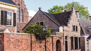 A historic brick building with a steeply pitched roof, a prominent chimney, and a small arched entrance. - Well Furnished Mobile Home with Dishwasher near Water (Gasselternijveen)