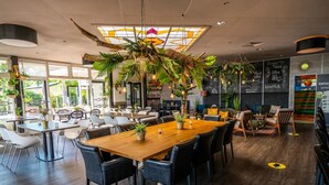 A modern restaurant with wooden tables and chairs, potted plants, and a large chandelier. - Comfortable Chalet With Dishwasher, Near the Sea in Egmond (Egmond aan den Hoef)