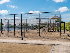 A fenced playground area with a wooden play structure and a small pavilion. - Comfortable Chalet With Dishwasher, Near the Sea in Egmond (Egmond aan den Hoef)