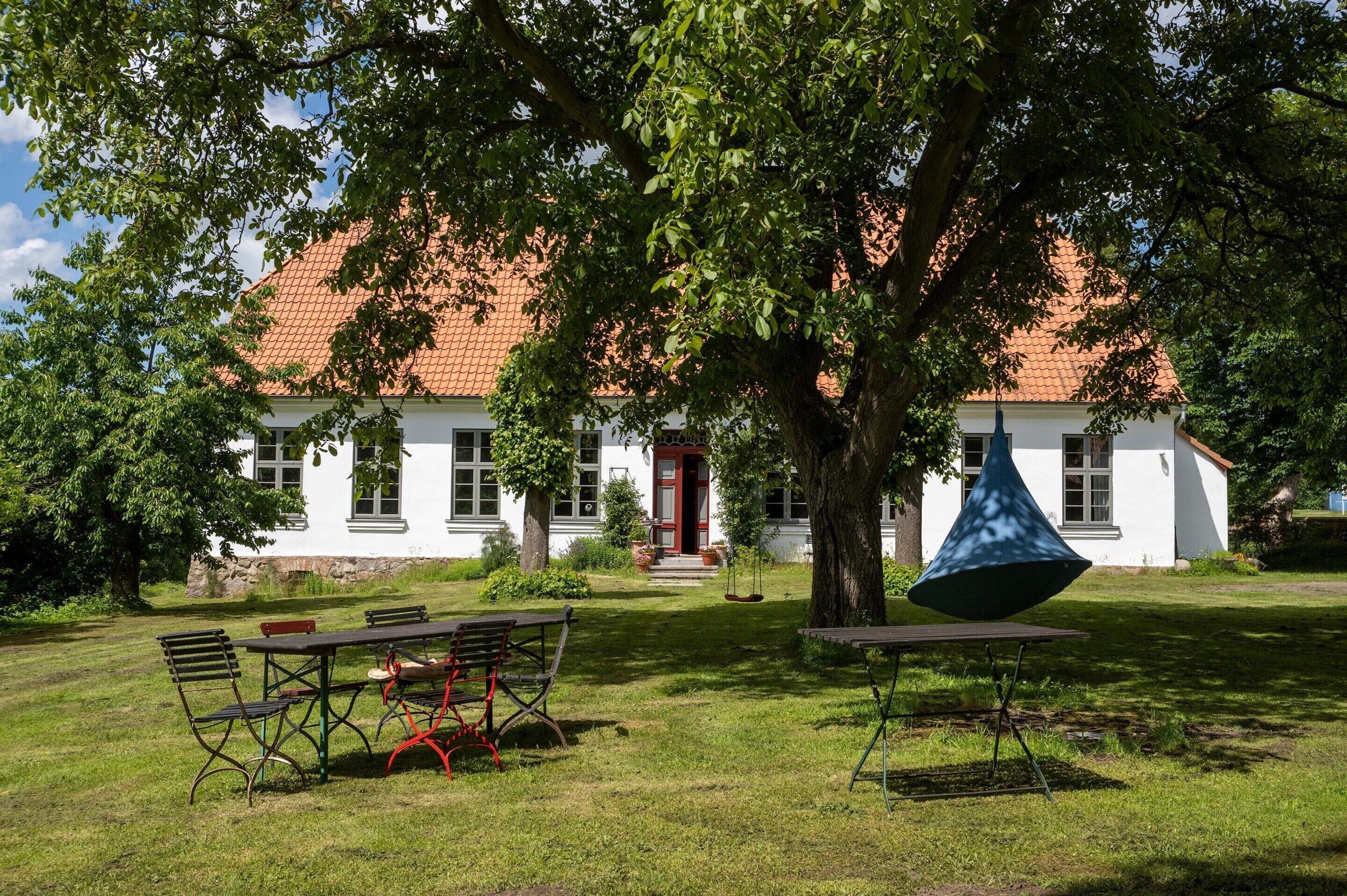 A white building with a red roof, surrounded by a grassy area with outdoor seating.