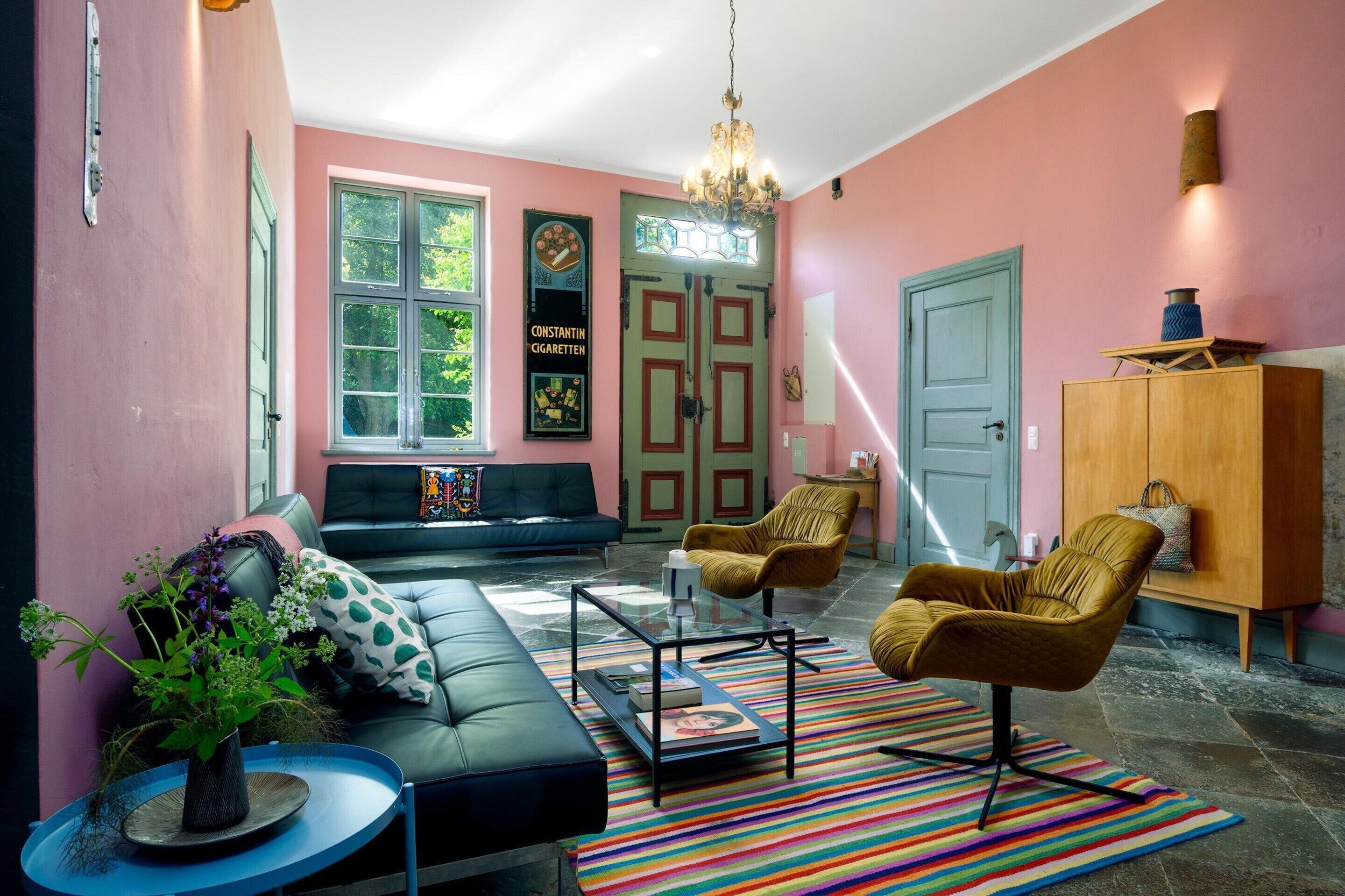 A living room with a black sofa, two armchairs, a coffee table, a colorful striped rug, and a bookshelf.