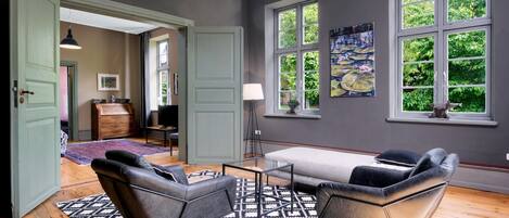 A room with a large window, a sofa, a patterned rug, and a painting on the wall.