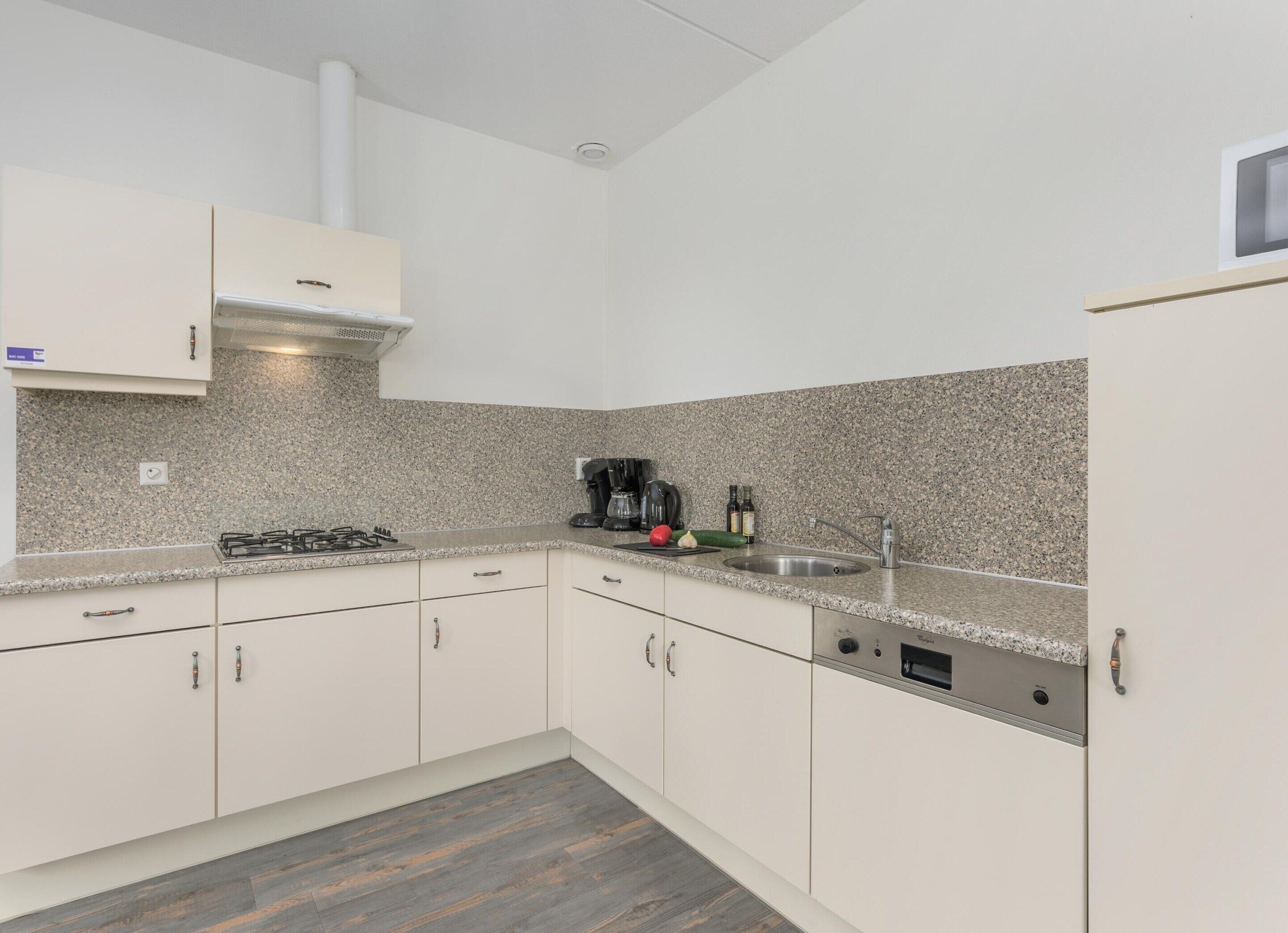 Eine moderne Küche mit weißen Schränken, Granit Arbeitsplatten, einem Gasherd, einer Kaffeemaschine und einem Spülbecken.