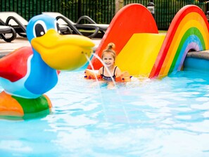 Ein Kind im Pool mit einer Schwimmdackel-Attrappe und einer Regenbogen-Rutsche.