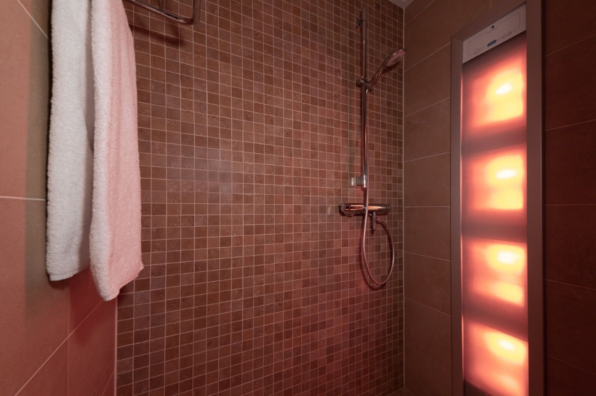 A shower area with a tiled wall, a towel rack, and a wall-mounted light fixture.