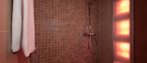 A shower area with a tiled wall, a towel rack, and a wall-mounted light fixture.