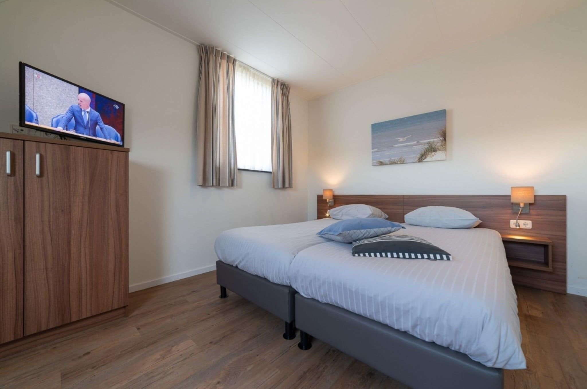 A bedroom with a bed, a TV on a cabinet, a painting on the wall, and a window with curtains.