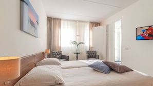 Una camera d'albergo con due letti, una TV, un vaso con fiori e un quadro appeso al muro.