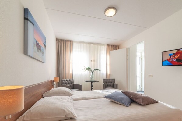 A hotel room with two beds, a TV, a vase with flowers, and a painting on the wall. - Holiday Home Near Dutch Beaches (Colijnsplaat)