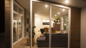 Una sala moderna con un sofá, una mesa de centro y un área de comedor visible a través de puertas correderas de vidrio.