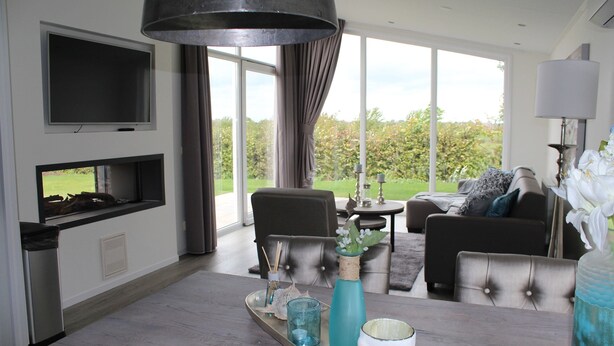 Un salón moderno con chimenea, un televisor montado en la pared y un amplio ventanal con vistas al exterior.