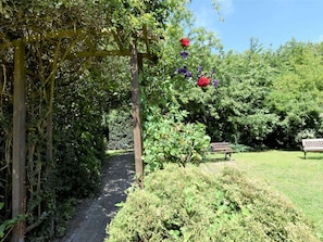 Stroll along the serene garden pathway, lined with lush greenery and vibrant flowers, and take a seat on the bench to unwind.