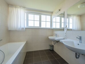A bathroom with a bathtub, two sinks, a mirror, and a window with curtains. - Bubble Bath Villa Escape (Bad Bentheim)