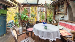 Un espace patio accueillant, avec une table et des chaises, entouré de plantes en pot et agrémenté de divers objets disposés sur des étagères.