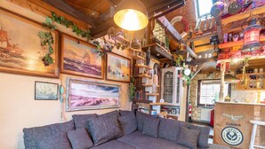 Un salon chaleureux avec un grand canapé d’angle, une table basse en bois et divers objets décoratifs, notamment des tableaux encadrés et des étagères ornées de bibelots.