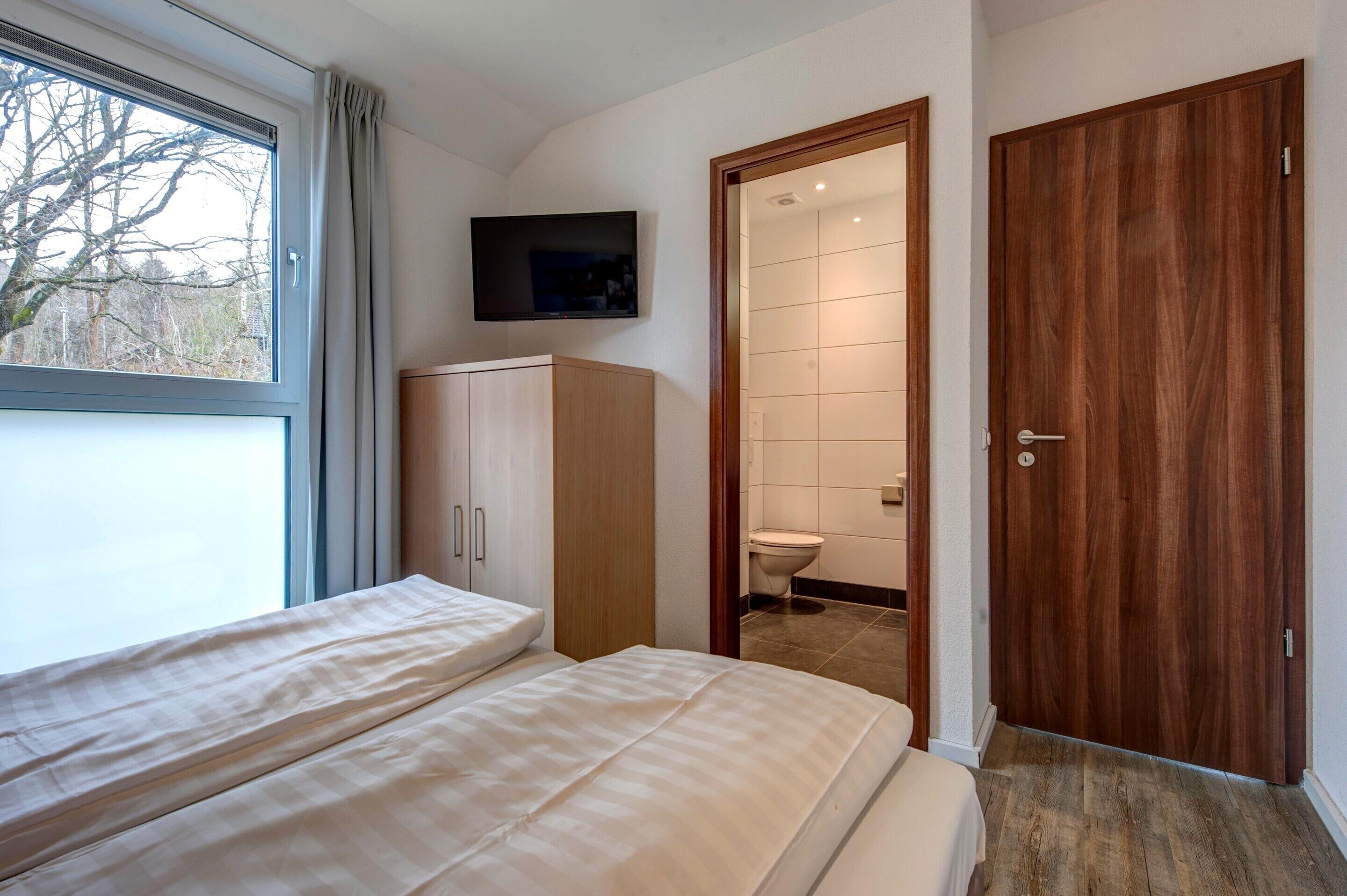 A bedroom with a bed, a wardrobe, a television, and a bathroom visible through an open door.