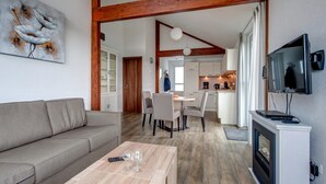 A modern living room with a sofa, a coffee table with glasses, a fireplace, and a TV mounted on the wall. - Single Storey Bungalow near Water Reservoir in Nordeifel (Dahlem)