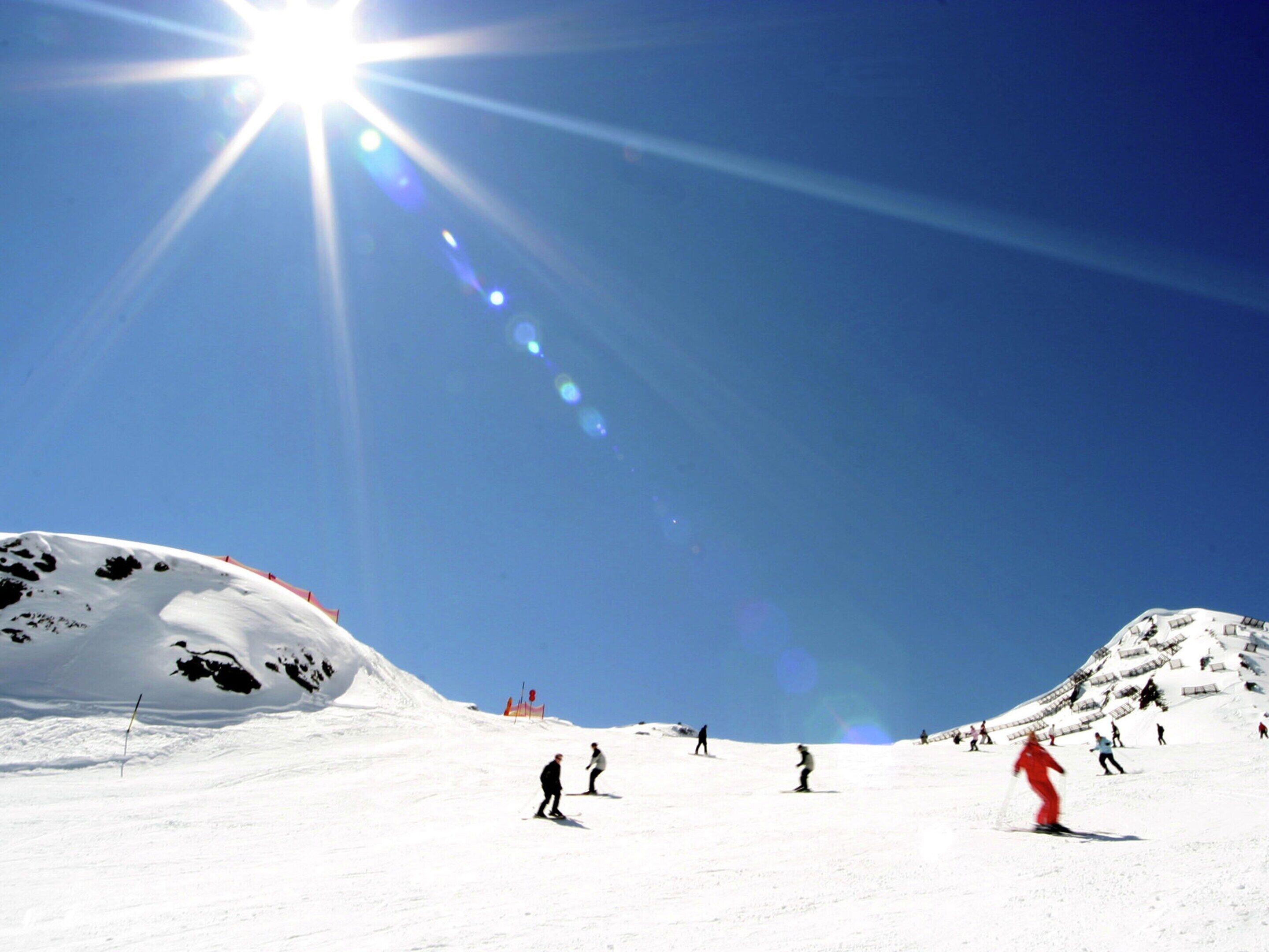 A snowy ski slope with skiers and a clear blue sky.