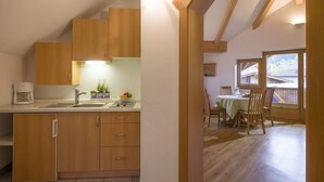 Une cuisine compacte avec des meubles en bois, une machine à café et un évier. On y trouve également un coin repas avec une table et des chaises, ainsi qu’une fenêtre donnant sur l’extérieur.