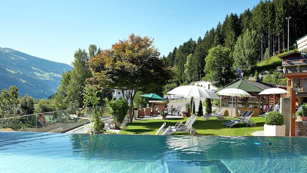 Une piscine à l’eau claire, entourée de chaises longues et de parasols, avec en arrière-plan des arbres et une montagne.