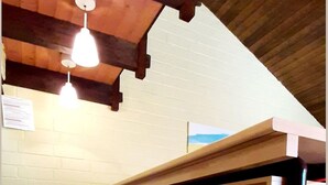 A kitchen with a wooden ceiling, white brick walls, and a tiled floor. There is a shelf unit with a black frame and a hanging light fixture. - Ferienhaus im Hochsauerland mit Terrasse (Bestwig)