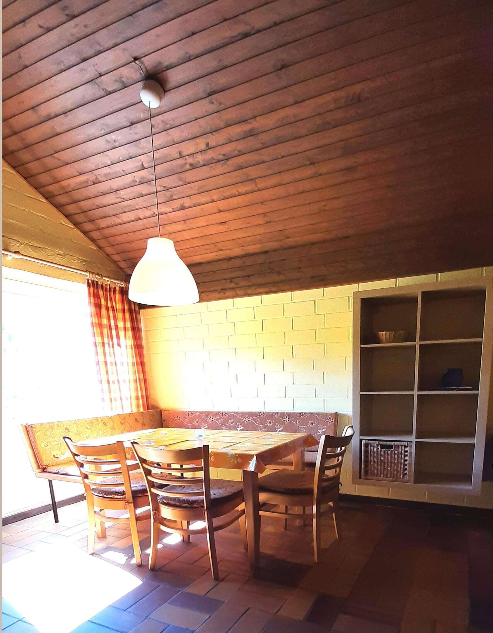 Uma área de refeições com uma mesa e cadeiras de madeira, um lustre pendurado, uma parede de tijolos e uma estante embutida.