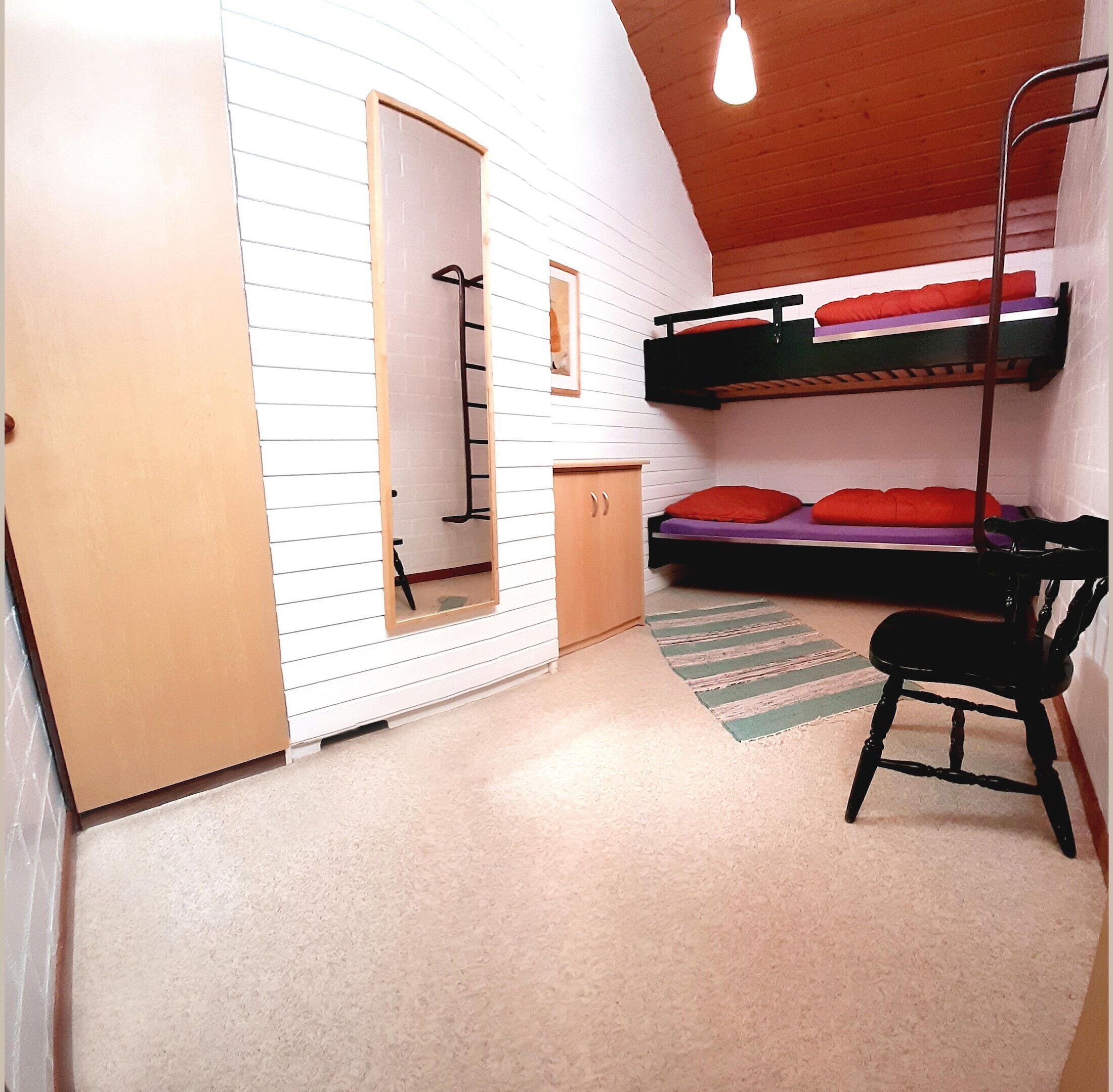 A compact room with bunk beds, a small wooden cabinet, a ladder, and a chair.