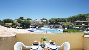 A balcony with a table set for breakfast overlooking a swimming pool, surrounded by umbrellas and greenery. - Peaceful Stay Among Pines (Agde)