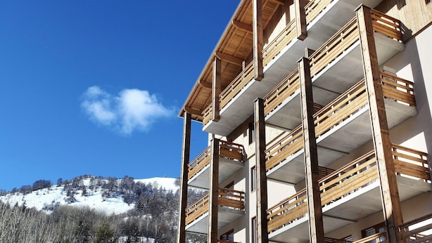 Un edificio de varios pisos con balcones, un cielo azul despejado y una colina nevada al fondo.