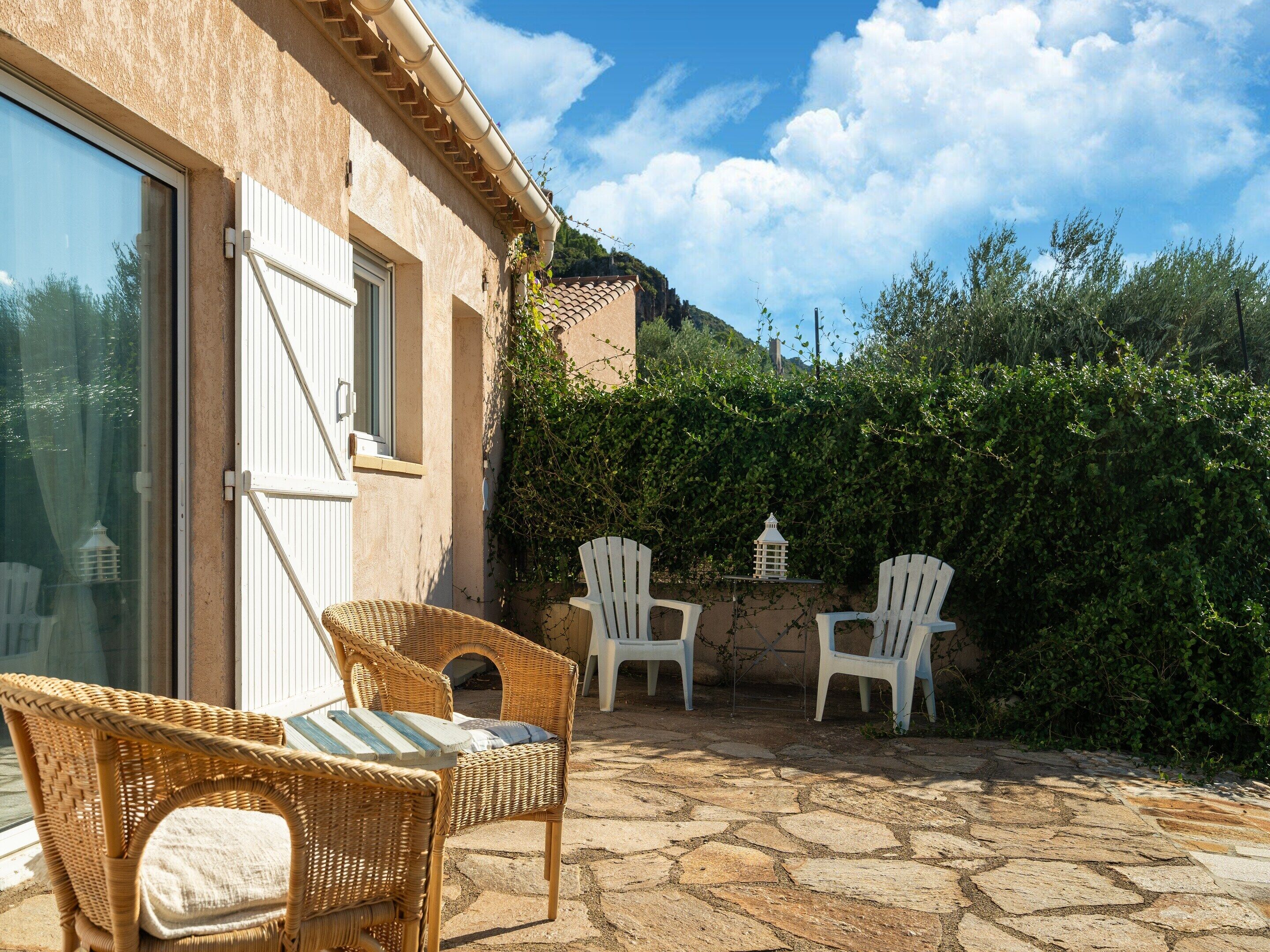 A patio with wicker chairs and a table, a stone floor, and a view of a hillside.