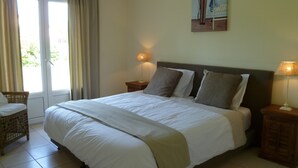Ein ordentlich bezogenes Bett mit Kopfteil, zwei Nachttischlampen, ein Korbstuhl und ein Fenster mit Vorhängen.