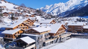 Un complejo turístico en la montaña cubierto de nieve, con edificios de madera, pistas de esquí y una vista despejada de las montañas.