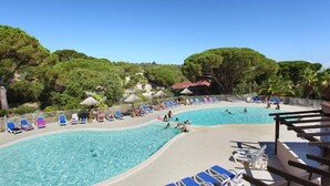 Ein Poolbereich mit Liegestühlen und Sonnenschirmen, umgeben von Bäumen und wolkenlosem Himmel.