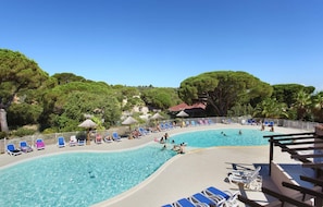 A pool area with lounge chairs and umbrellas, surrounded by trees and a clear sky. - Spacious Apt Near the Beach (Fréjus)
