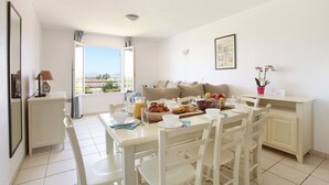 Ein heller, offener Wohnbereich mit Esstisch, gedeckter für ein Frühstück, einer Couch und einem Balkon mit Blick.