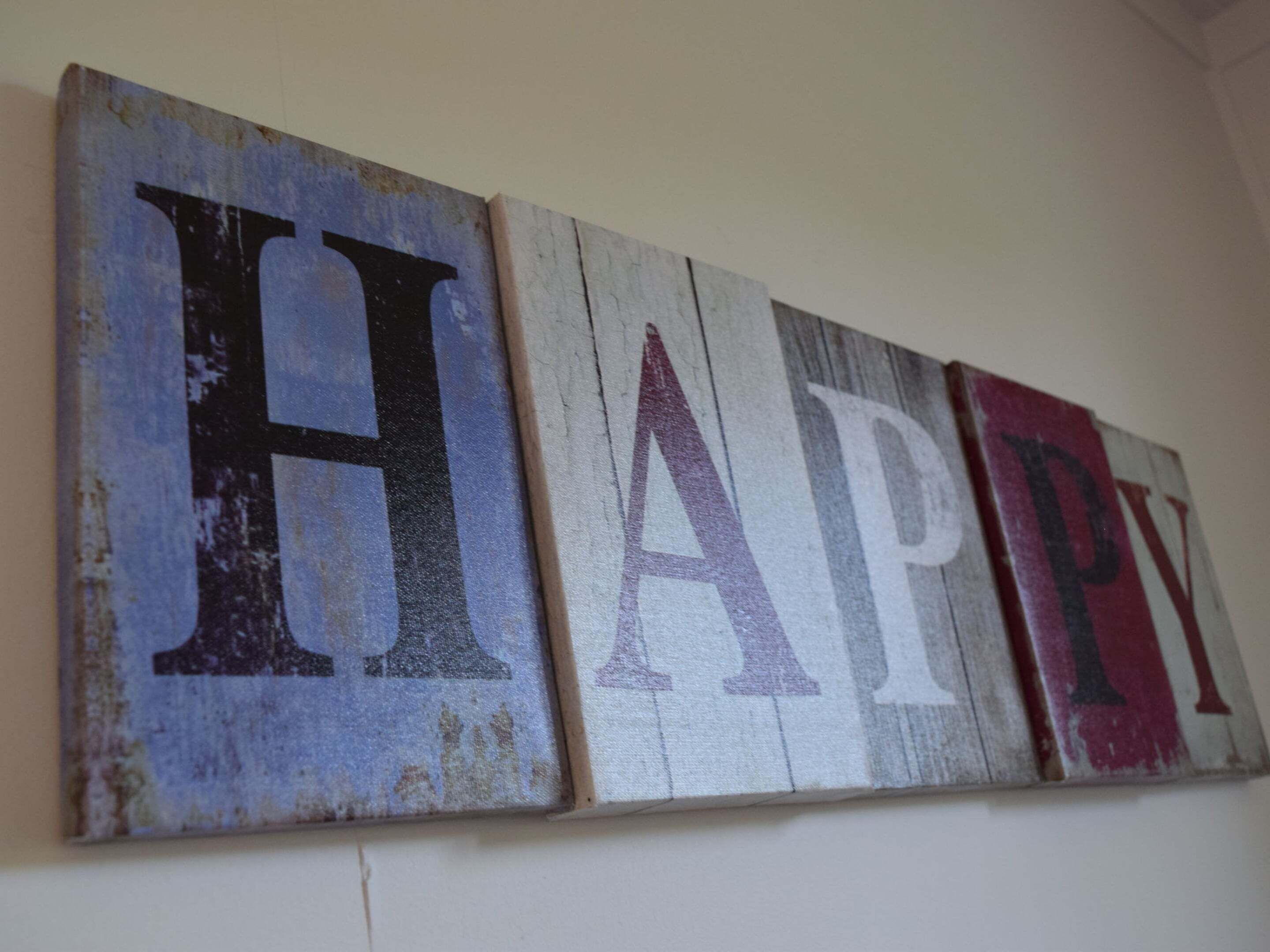 A wall with three wooden panels displaying the letters H, A, P, and Y in large, distressed fonts.