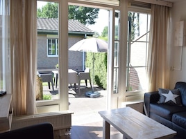 A room with a large sliding glass door leading to an outdoor patio with a table and chairs, a radiator, and a sofa with a star pillow.