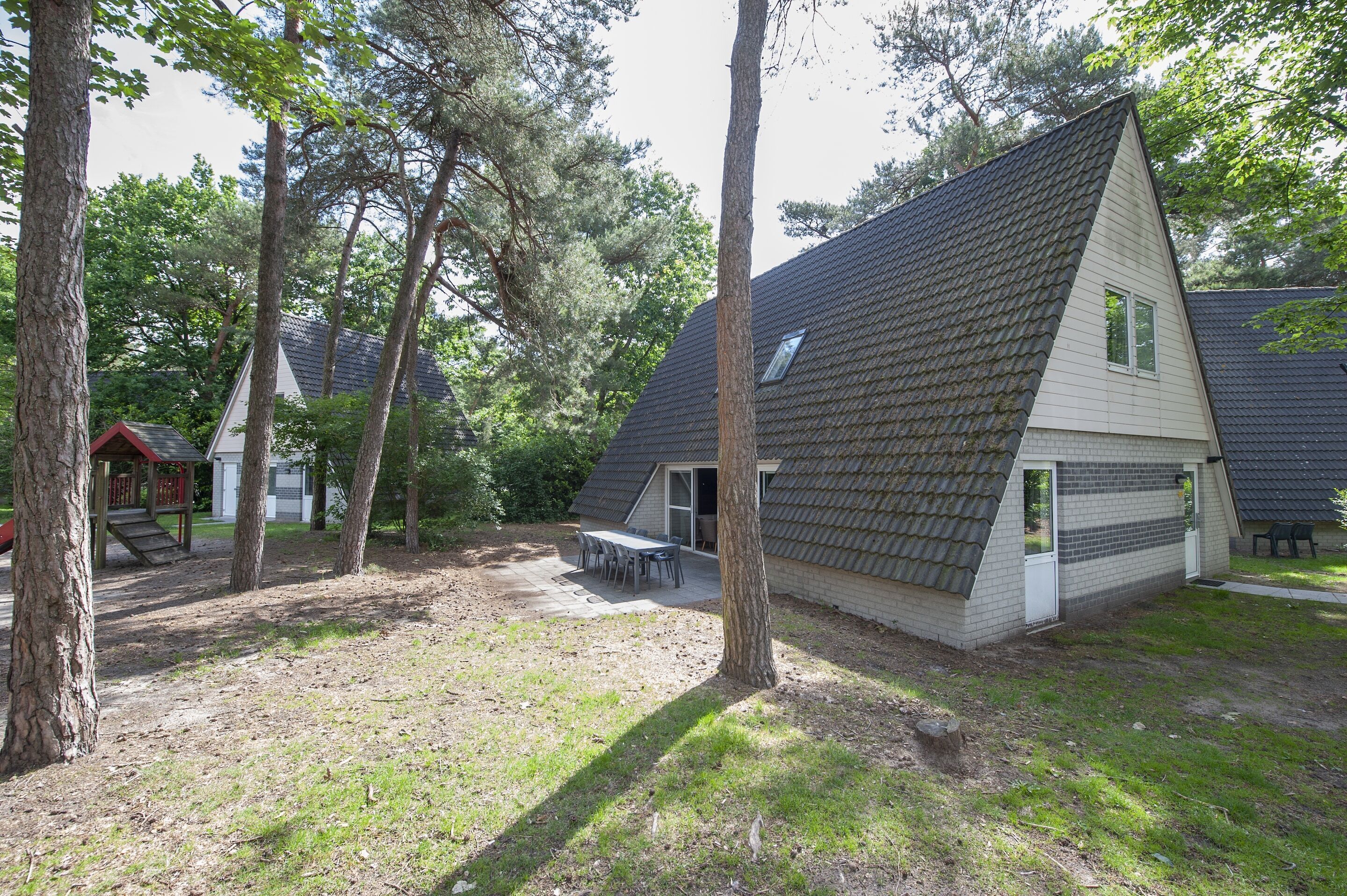 A house with a sloped roof, a patio with a table and chairs, and a small deck.