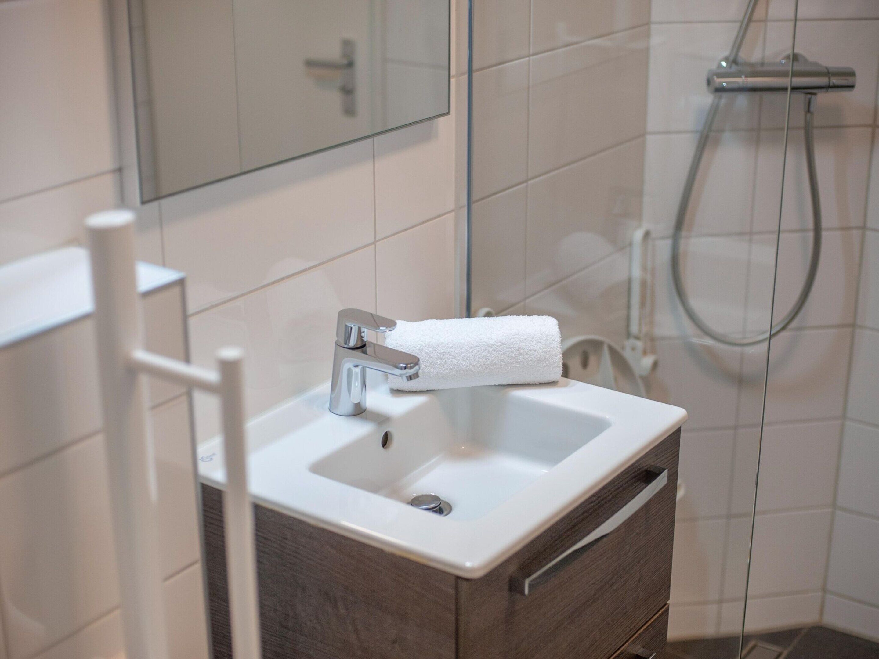 A bathroom with a white sink, a towel, a mirror, and a shower.