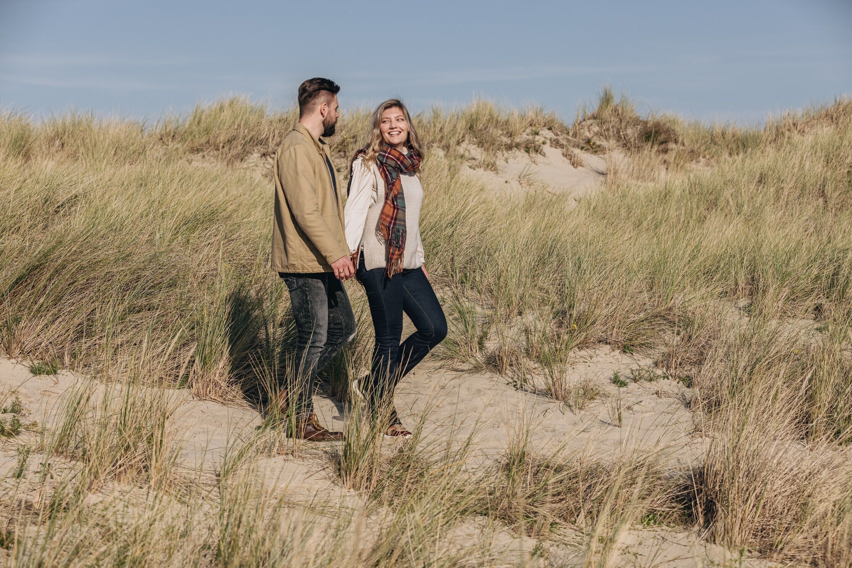 A couple standing on sand dunes with grass around them.