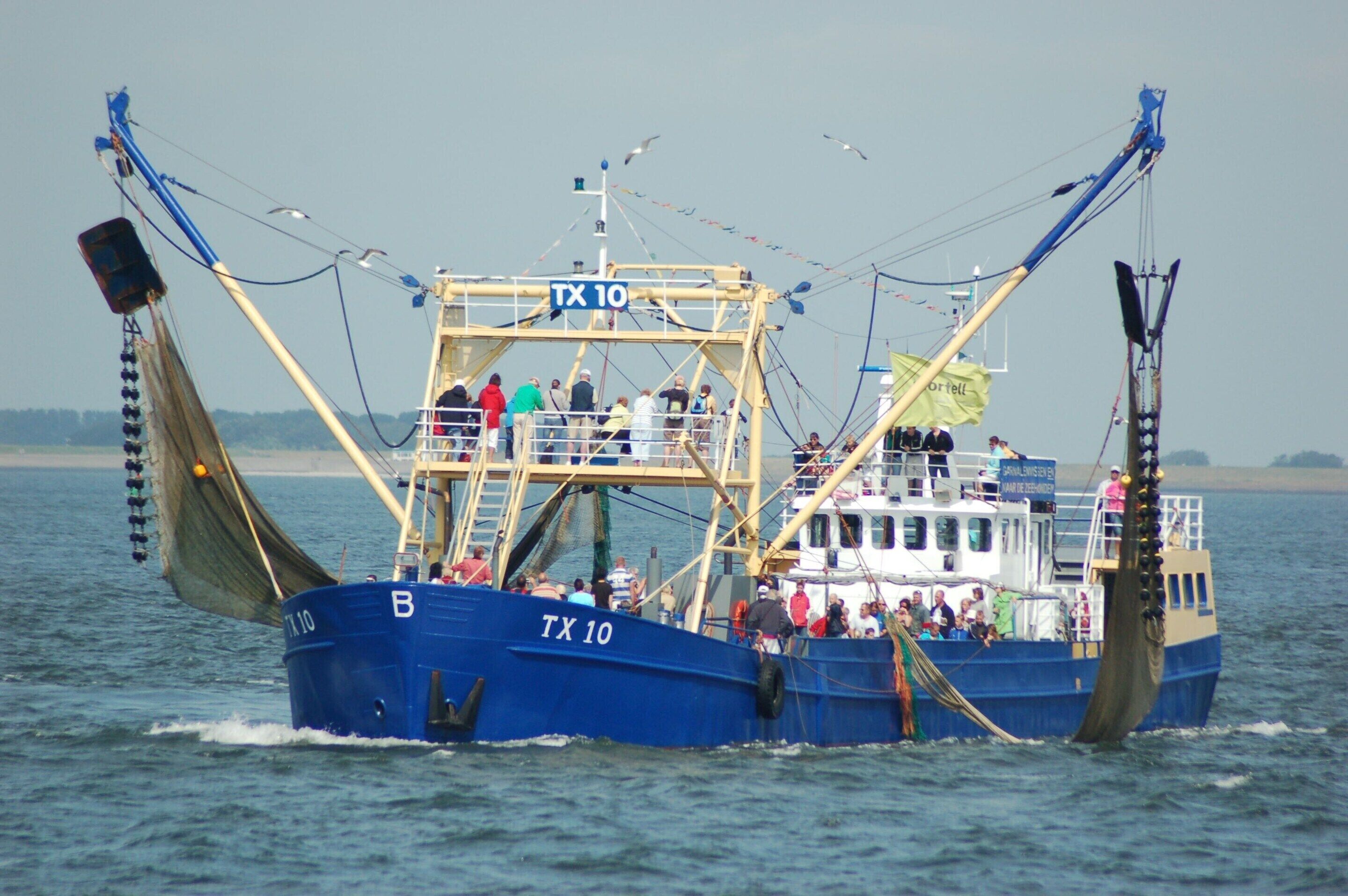 Un gran barco pesquero con el nombre "TX 10" en su costado, equipado con redes de pesca y una grúa, navegando sobre el agua.
