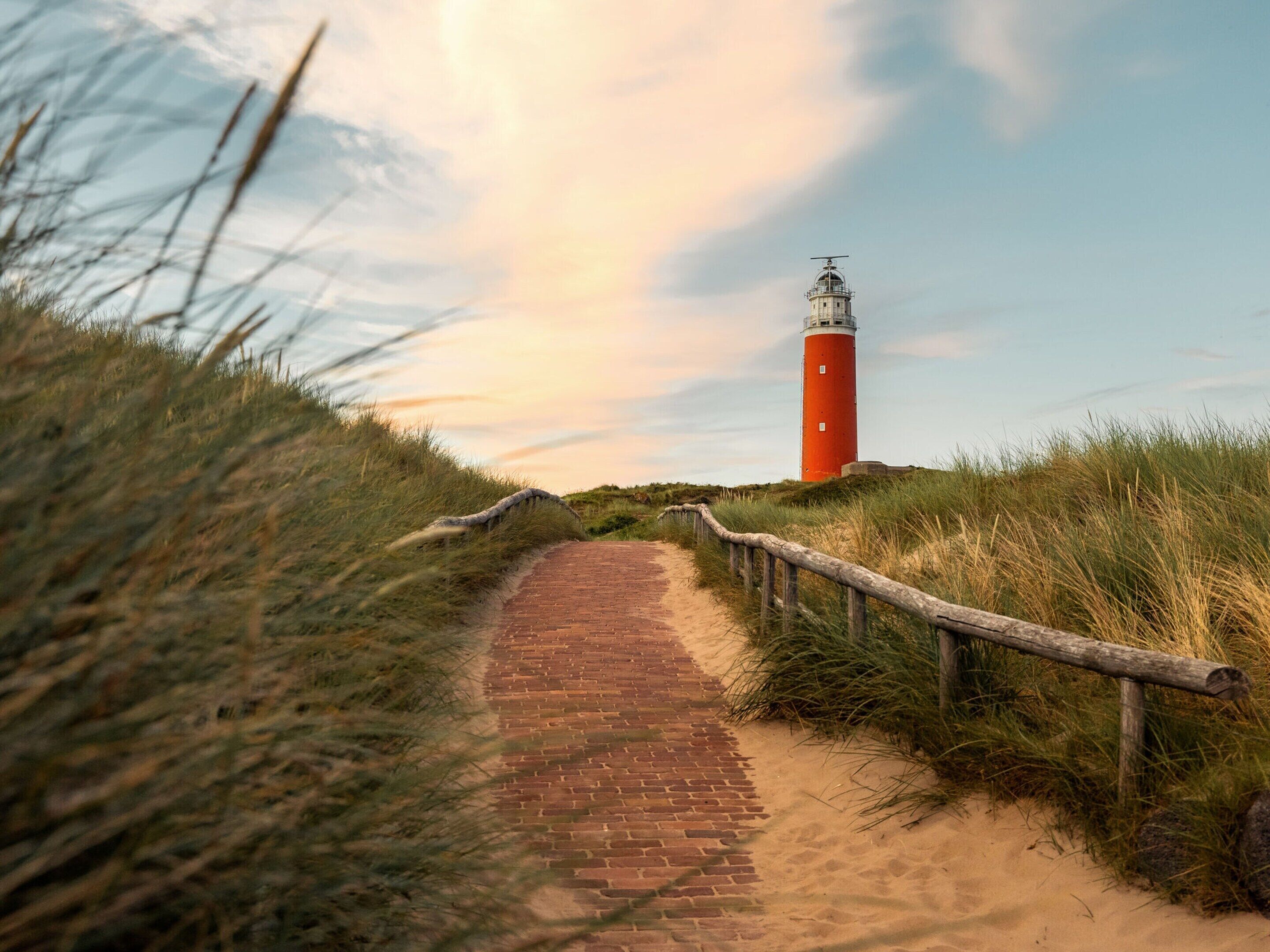A brick pathway leading to a red lighthouse.
