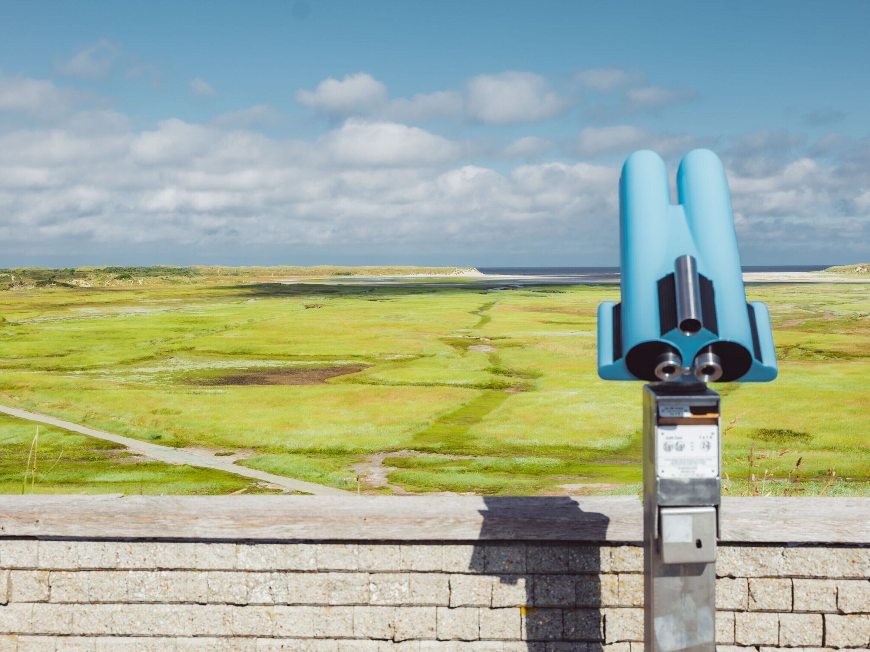 A telescope on a stone platform overlooking a green landscape with a cloudy sky.