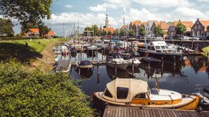 A marina with various boats docked, surrounded by buildings with red roofs and a prominent tower in the background. - Luxury Chalet Near Beach (Kamperland)