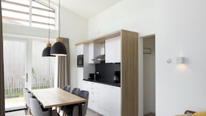 A modern kitchen with white cabinets, a wooden countertop, and a dining area with a table and chairs. - Luxury Chalet Near Beach (Kamperland)
